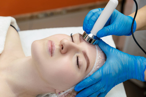 Jeune femme obtient cavitation faciale dans le salon de spa. Amélioration du contour du visage dans le salon de beauté. - Photo, image