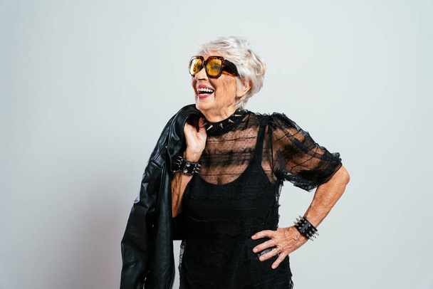 schöne und elegante alte Influencerin. Coole Großmutter posiert in modischer Kleidung im Studio. Glückliche Seniorin feiert und macht Party. Konzept zu Dienstalter und Lebensstil - Foto, Bild