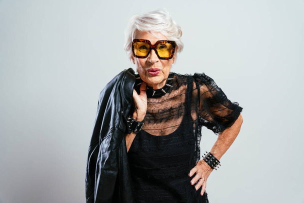Beautiful and elegant old influencer woman. Cool grandmother posing in studio wearing fashionable clothes. Happy senior lady celebrating and making party. Concept about seniority and lifestyle - Foto, afbeelding
