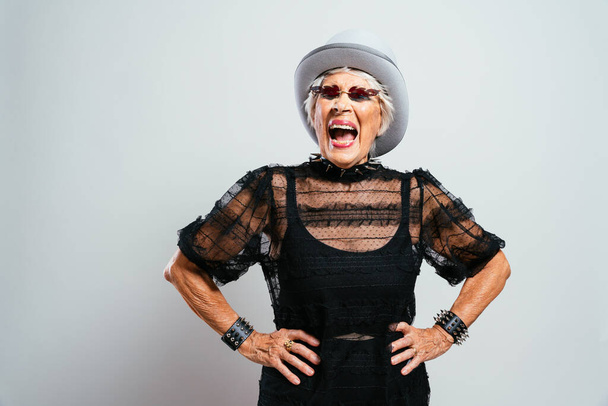 beautiful and elegant old influencer woman. Cool grandmother posing in studio wearing fashionable clothes. Happy senior lady celebrating and making party. Concept about seniority and lifestyle - Fotografie, Obrázek