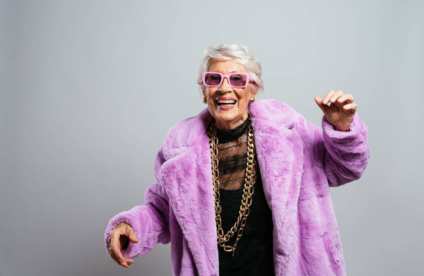 image of a beautiful and elegant old influencer woman. Cool grandmother posing in studio wearing fashionable clothes. Happy senior lady celebrating and making party. Concept about seniority and lifestyle - Фото, зображення