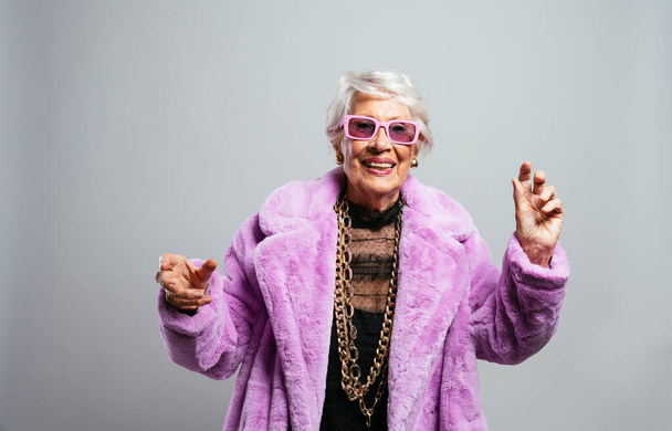 image of a beautiful and elegant old influencer woman. Cool grandmother posing in studio wearing fashionable clothes. Happy senior lady celebrating and making party. Concept about seniority and lifestyle - Photo, Image