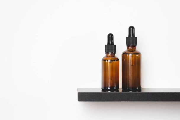 Amber glass dropper bottles with black lid on the shelf. Skincare concept on whte wall background. Spa natural cosmetic concept for face body care - Valokuva, kuva