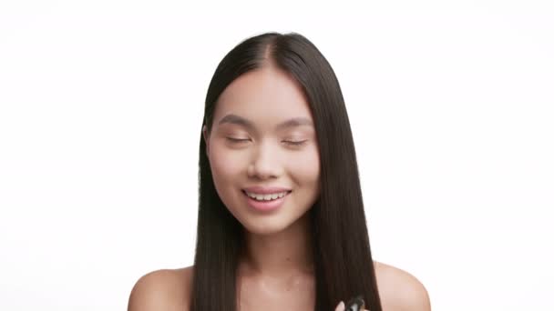 Japanilainen nainen ruiskuttamalla hiuslakkaa Pitkät hiukset poseeraa valkoisella taustalla - Materiaali, video
