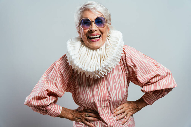 beautiful and elegant old influencer woman. Cool grandmother posing in studio wearing fashionable clothes. Happy senior lady celebrating and making party. Concept about seniority and lifestyle - Zdjęcie, obraz