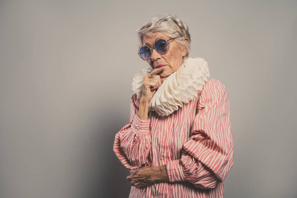 beautiful and elegant old influencer woman. Cool grandmother posing in studio wearing fashionable clothes. Happy senior lady celebrating and making party. Concept about seniority and lifestyle - Foto, Imagen
