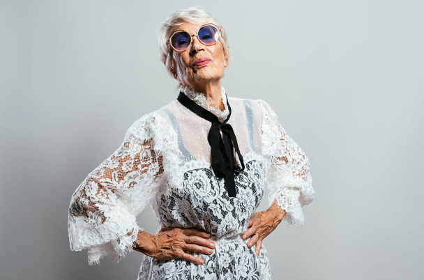 beautiful and elegant old influencer woman. Cool grandmother posing in studio wearing fashionable clothes. Happy senior lady celebrating and making party. Concept about seniority and lifestyle - 写真・画像