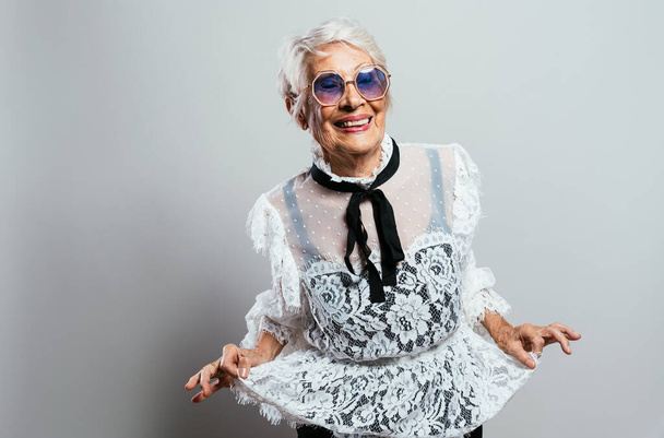 beautiful and elegant old influencer woman. Cool grandmother posing in studio wearing fashionable clothes. Happy senior lady celebrating and making party. Concept about seniority and lifestyle - Fotoğraf, Görsel