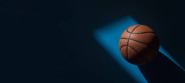 Brown new basketball ball with natural lighting on blue background. Sport team concept. Horizontal sport theme poster, greeting cards, headers, website and app - Photo, image