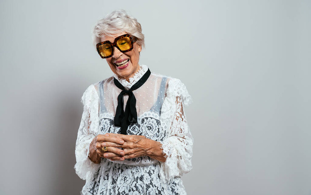 beautiful and elegant old influencer woman. Cool grandmother posing in studio wearing fashionable clothes. Happy senior lady celebrating and making party. Concept about seniority and lifestyle - Фото, зображення
