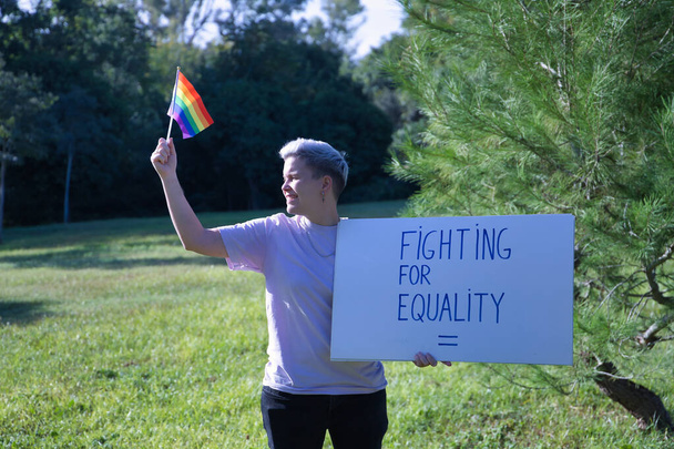 Non-binary person, with gay pride flag and sign with text, fighting for equality. Non-binary concept, lgbtq+, inclusion, gay, lesbian, lgbtq. - Foto, imagen