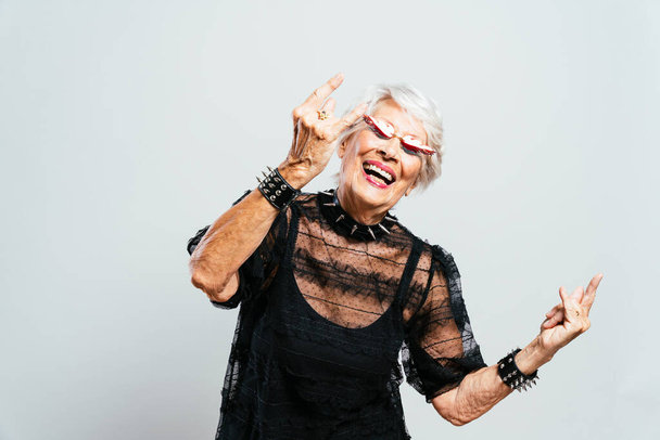 Beautiful and elegant old influencer woman. Cool grandmother posing in studio wearing fashionable clothes. Happy senior lady celebrating and making party. Concept about seniority and lifestyle - Foto, afbeelding