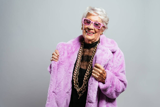 image of a beautiful and elegant old influencer woman. Cool grandmother posing in studio wearing fashionable clothes. Happy senior lady celebrating and making party. Concept about seniority and lifestyle - Fotó, kép