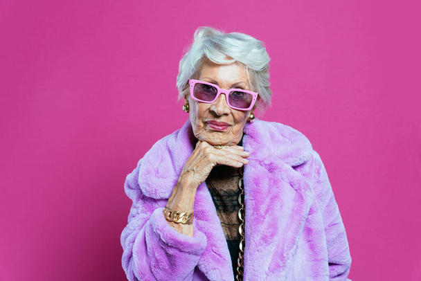 image of a beautiful and elegant old influencer woman. Cool grandmother posing in studio wearing fashionable clothes. Happy senior lady celebrating and making party. Concept about seniority and lifestyle - Valokuva, kuva