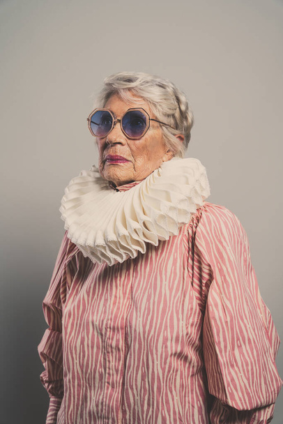 beautiful and elegant old influencer woman. Cool grandmother posing in studio wearing fashionable clothes. Happy senior lady celebrating and making party. Concept about seniority and lifestyle - Fotó, kép