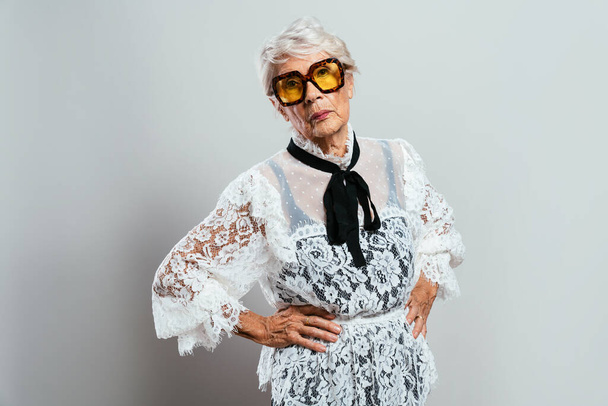 beautiful and elegant old influencer woman. Cool grandmother posing in studio wearing fashionable clothes. Happy senior lady celebrating and making party. Concept about seniority and lifestyle - Foto, immagini