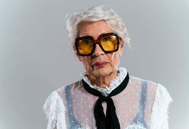 beautiful and elegant old influencer woman. Cool grandmother posing in studio wearing fashionable clothes. Happy senior lady celebrating and making party. Concept about seniority and lifestyle - Photo, Image