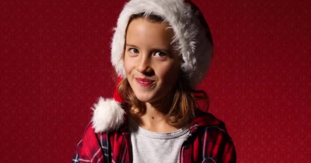 Retrato de la niña de Navidad en Santa Sombrero, tratando de ser serio pero sonreír, reír - Metraje, vídeo