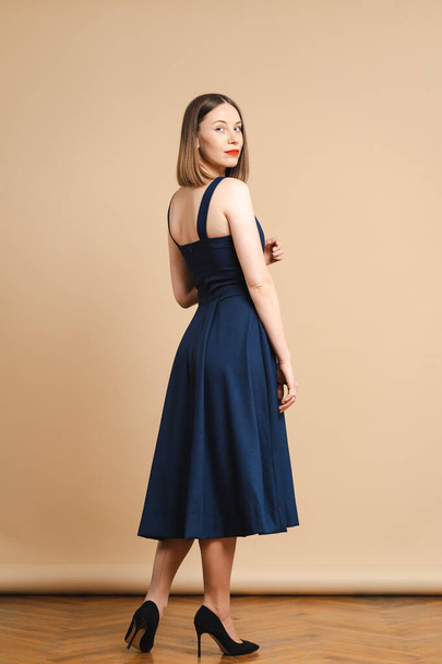 美しい女性かわいい顔明るい顔ケアダークブロンドの髪の服短い青ドレスでベージュの背景 - 写真・画像