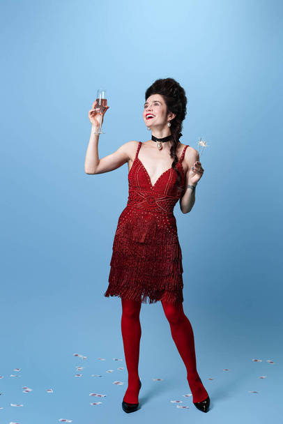 Портрет молодої чарівної чудової жінки в темно-червоній, вечірній сукні кольору вина, що святкує свято ізольовано на синьому фоні
. - Фото, зображення