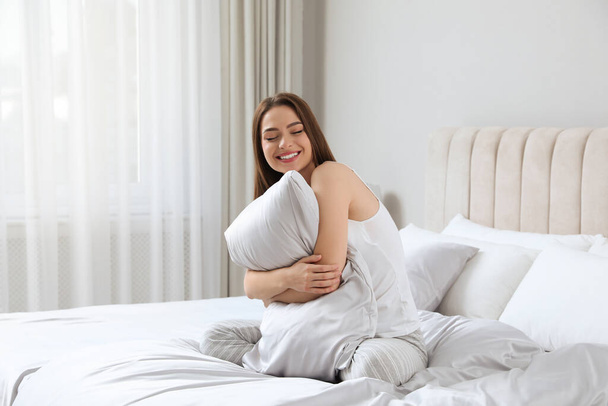 Giovane donna che abbraccia cuscino su un comodo letto con biancheria di seta - Foto, immagini
