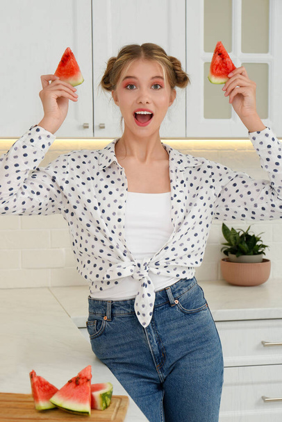 Emotional teenage girl with slices of watermelon near countertop in kitchen - 写真・画像