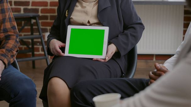 Nahaufnahme eines Psychologen, der bei einem Gruppentreffen einen horizontalen grünen Bildschirm auf dem Tablet zeigt - Foto, Bild