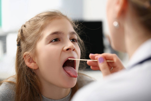Ragazzina che si fa esaminare la gola con un cucchiaio speciale da un medico donna in ospedale - Foto, immagini