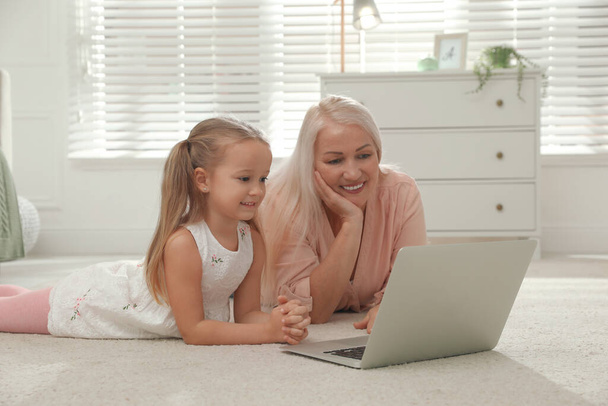 Happy grandmother and her granddaughter using  laptop together on floor at home - Foto, afbeelding