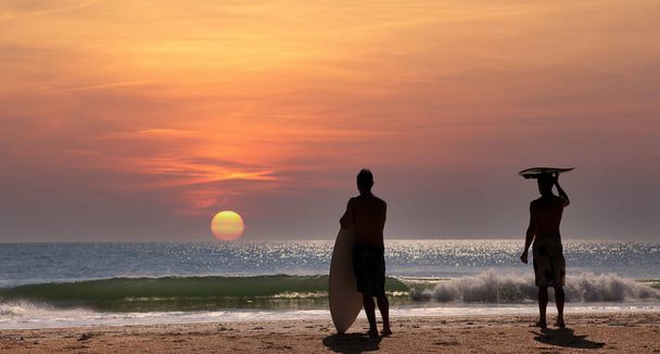 Dwóch surferów czeka na falę w Cocoa Beach na Florydzie, USA, o zachodzie słońca - Zdjęcie, obraz
