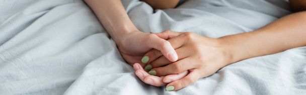 cropped view of young lesbian women holding hands on bed, banner - Фото, зображення