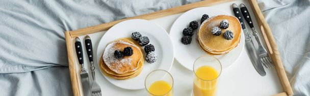 high angle view of blackberries on tasty pancakes near glasses on orange juice on tray, banner - Photo, Image