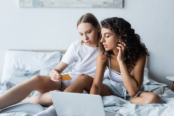 молодая лесбийская пара смотрит на ноутбук в то время как онлайн покупки из дома  - Фото, изображение