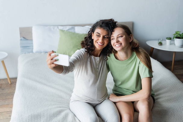 pregnant woman taking selfie with happy girlfriend in bedroom - Φωτογραφία, εικόνα