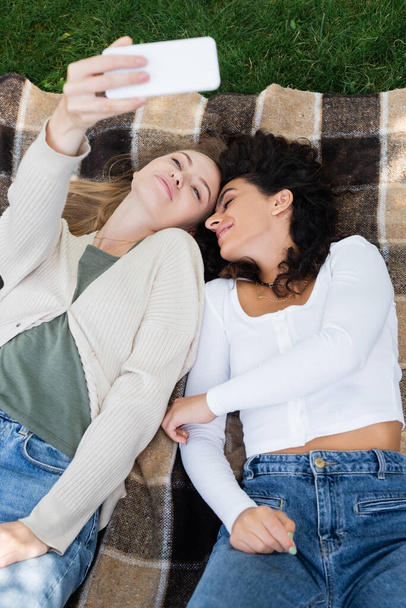 high angle view of women taking selfie while lying on plaid blanket  - Φωτογραφία, εικόνα