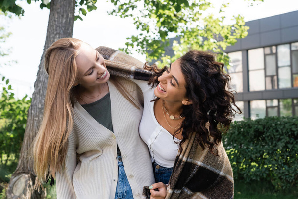 feliz lesbiana pareja cubierto en manta riendo mientras mirándose fuera  - Foto, Imagen
