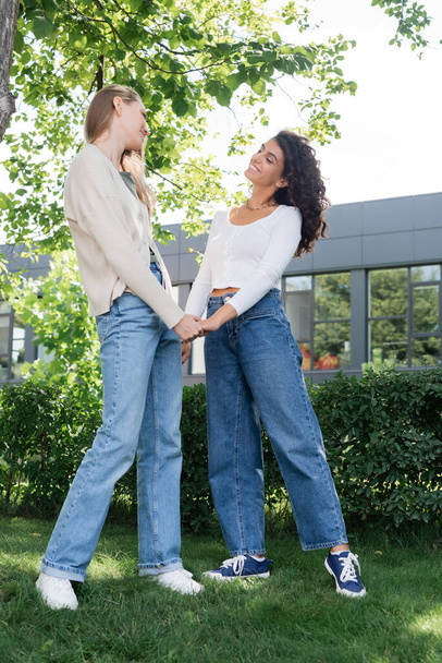 full length of pleased lesbian couple holding hands outside  - Foto, afbeelding