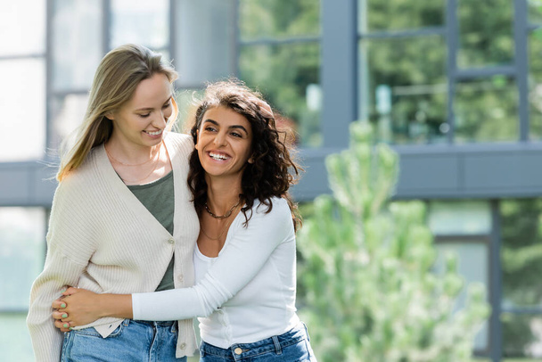 curly woman smiling while hugging girlfriend outside  - Foto, Bild