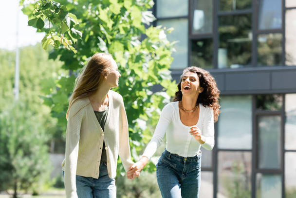 pleased lesbian couple holding hands and laughing outside  - Foto, imagen