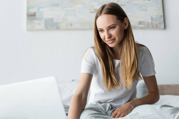 pleased young freelancer using laptop in bedroom - Photo, Image