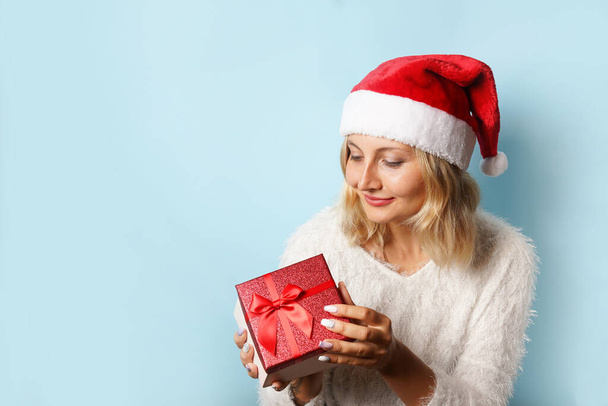 karácsony, téli mosolygós nő télapó kalap piros ajándék doboz kék háttér - Fotó, kép