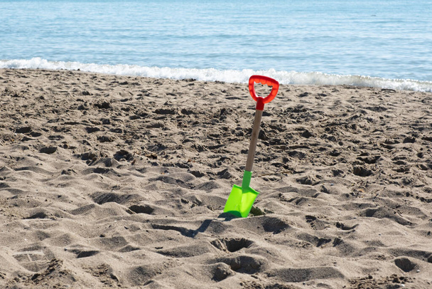 Plastic children's toy on a deserted sandy beach. A shovel in the sand. The end of tourist season. - Foto, Imagem