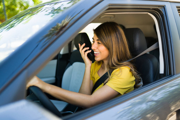 Захоплена молода жінка розмовляє по телефону по гучномовцю і сміється під час водіння своєї машини
 - Фото, зображення