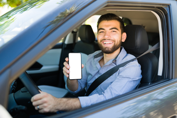 Młody człowiek za kierownicą pracuje jako kierowca w aplikacji mobilnej Rideshare i pokazuje swój ekran smartfona - Zdjęcie, obraz
