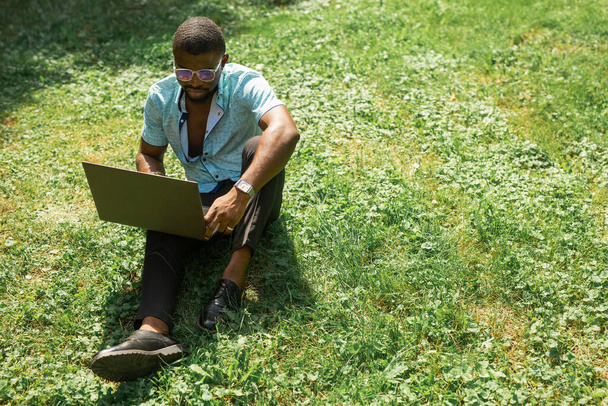 handsome african man resting sitting on the grass in the park with a laptop - Fotoğraf, Görsel