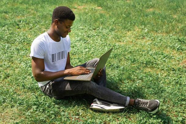 working african male with laptop on the grass in summer - Foto, immagini
