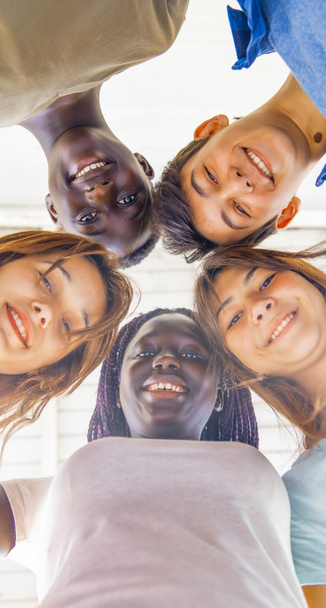 Pohled nahoru na teenagery, jak se spolu usmívají v kruhu. Multietničtí přátelé šťastný, freindship a antiracism koncept. - Fotografie, Obrázek