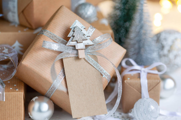 Holiday gift box. Christmas present with address card tag under fir tree on floor in room. Christmas and New Year concept. - Foto, Imagen