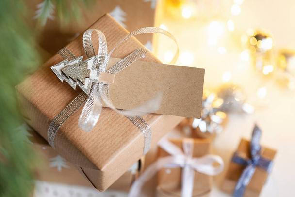 Holiday gift box. Christmas present with address card tag under fir tree on floor in room. Christmas and New Year concept. - Zdjęcie, obraz