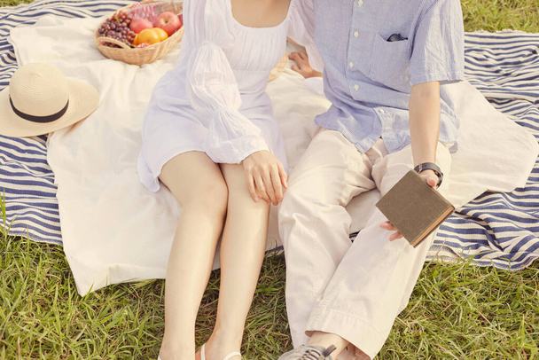 picnic concept The woman with white skirt and sandals sitting beside the man who puts on beige pants and grey sneakers. - Photo, Image